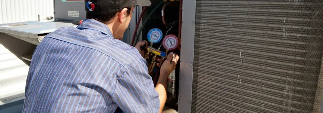 HVAC technician servicing a condenser unit in Wellston